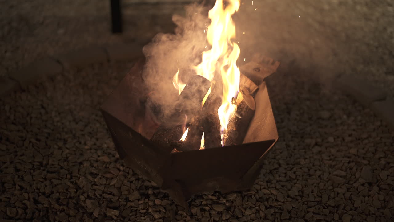 Utepeis som brenner med livlige flammer og røyk om natten, og gir varme og en koselig atmosfære for avslappet utendørs matlaging og sosialt samvær