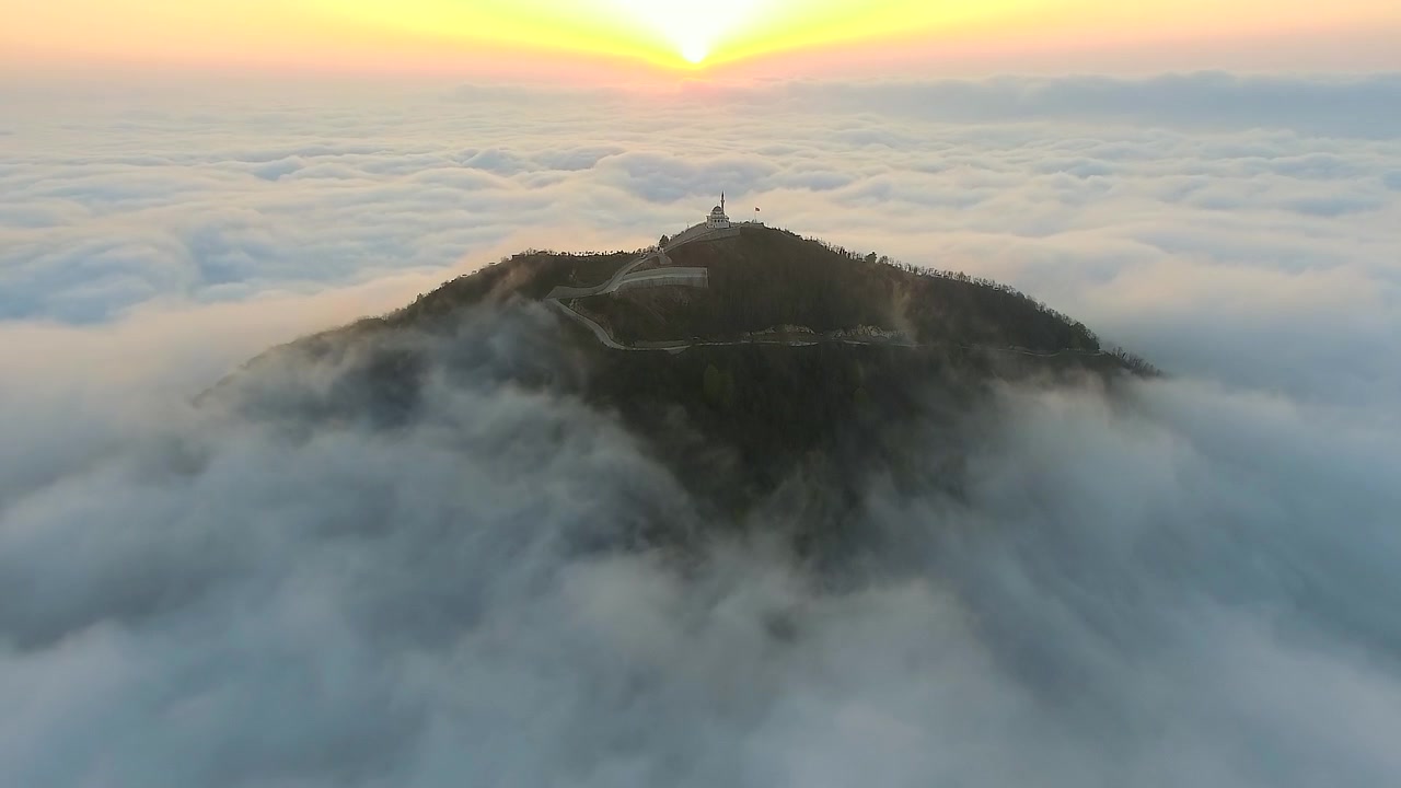 日の出時の雲海の上にそびえる山頂の空撮