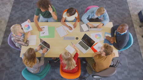 overhead shot of university or college students sitting around table with tutors in lesson