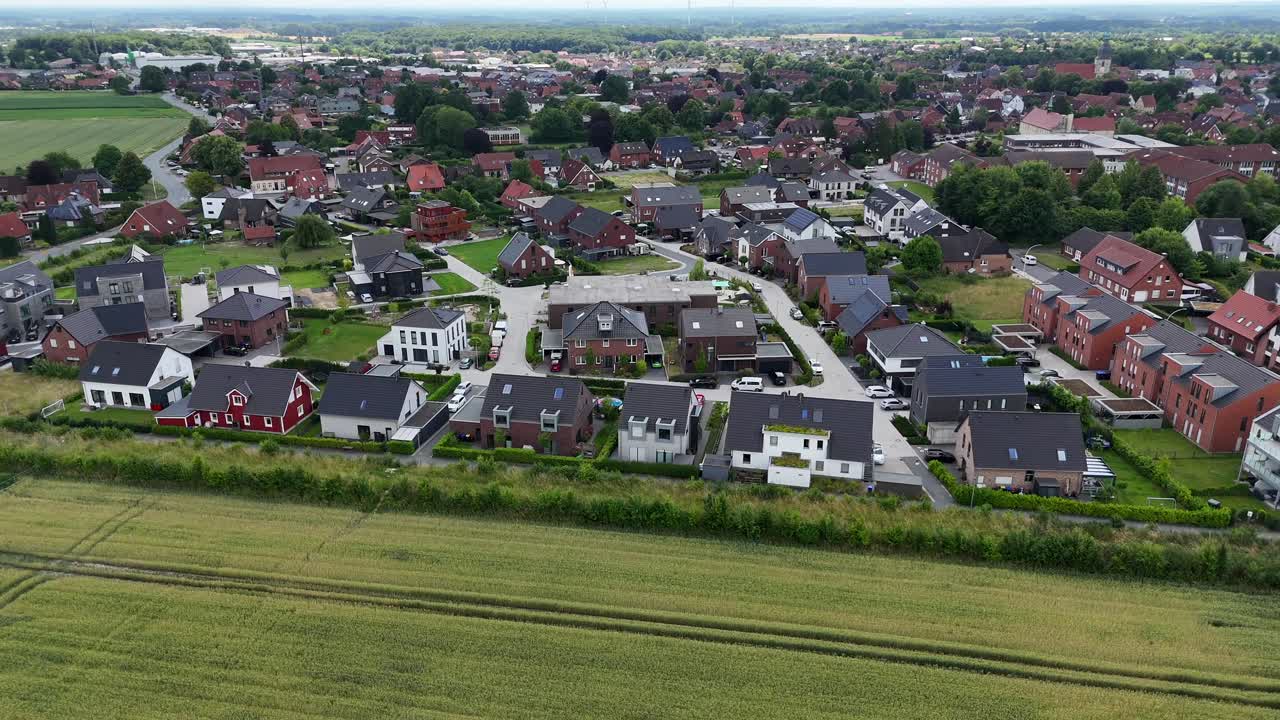 Single family houses in Suburb of town along green agricultural fields in summer. Aerial lateral wide shot. Two-story homes in German district of city. Wide shot. Summer season. Peaceful scene.