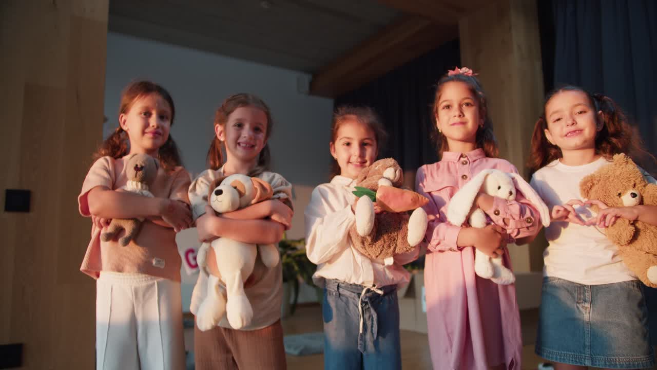 Zoom Out portrait of five preschool age girls with their soft toys standing and looking at the camera and smiling in a club room for preparing children for school