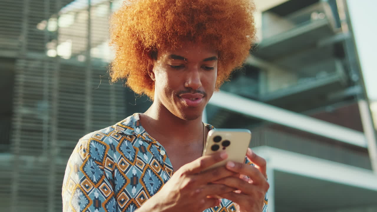 Young Man with Curly Hair Using Smartphone Outdoors