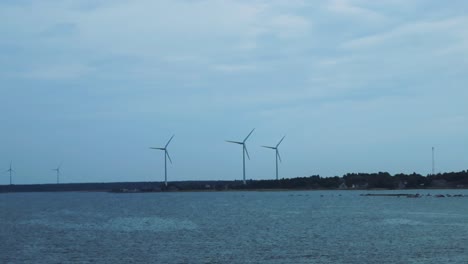 wind turbines that harness renewable energy form the wind in estonia coastline during summer time while the sky is cloudy and it is windy