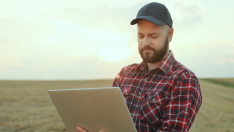 Close up of farmer wearing a shirt and black caseball cap looking at the sides and thiking while working on laptop computer