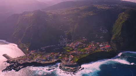 cinematic aerial shot of porto moniz surrounded by high mountains and blue atlantic ocean during sunset