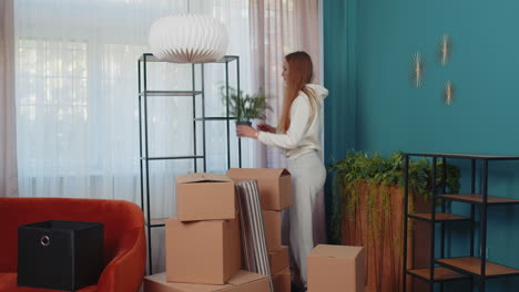 young woman unpacking cardboard boxes with interior furniture after buying new apartment home house