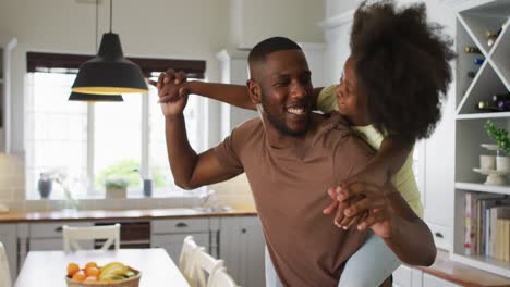 african american daughter on her father's back embracing him in kitchen