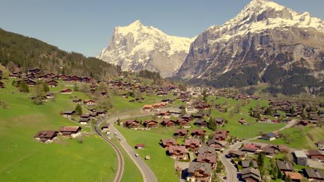 aerial drone footage pushing out with views of mountain train leaving grindelwald in swiss alps wide view