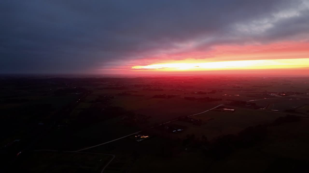 Drone video capturing a stunning sunrise with vivid colors over a vast, serene landscape. The aerial view showcases the horizon's warm glow, blending with the dark morning sky