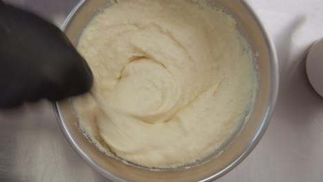 top down establishing shot of a gloved person's hand stirring flour dough in a bowl