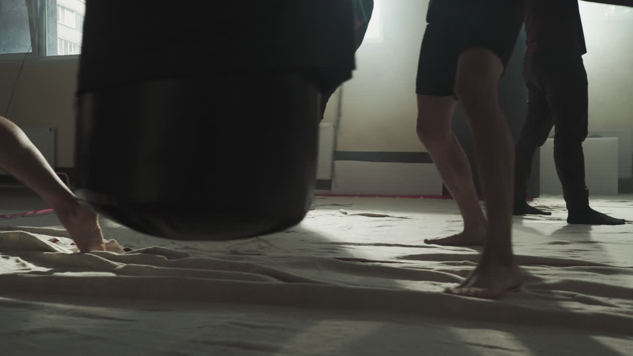 los luchadores ejercitan patadas en bolsas de boxeo en el gimnasio de primer plano. los kickboxers descalzos hacen un entrenamiento intenso con equipos pesados en el club de lucha en cámara lenta