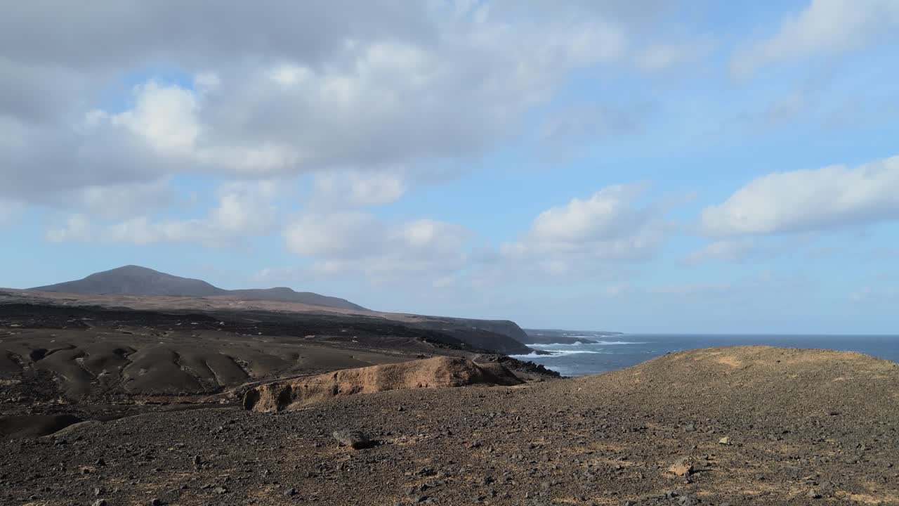 Black volcanic rocks cover the vast expanse of the lanzarote shore, creating a dramatic contrast with the deep blue of the atlantic ocean under a cloudy sky