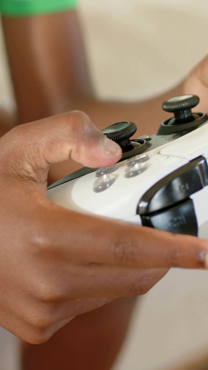 Vertical video: Zooming kid's hands playing game on couch with white controller green-white shirt