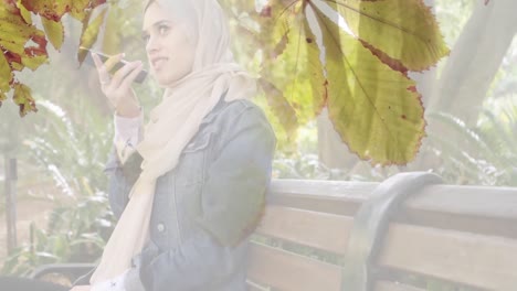 animation of asian woman in hijab using smartphone over leaves