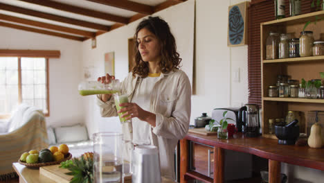 Feliz-Mujer-De-Raza-Mixta-Vertiendo-Bebida-Saludable-De-Pie-En-La-Cocina-De-La-Cabaña-Sonriendo