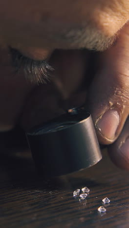 cu shot: bearded jeweler looks at small transparent gems through magnifier glass at wooden table extreme close view