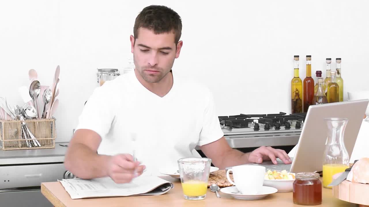 hombre trabajando con una computadora portátil en la cocina y desayunando