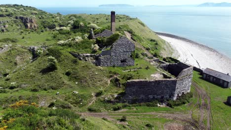 abandoned overgrown ivy covered desolate countryside historical welsh coastal brick factory mill aerial view rear push in