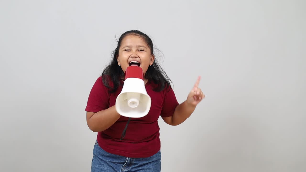 Energetic Adorable Asian girl enthusiastically shouts into a megaphone with a bright smile perfect for marketing campaigns promoting announcements and positive messaging