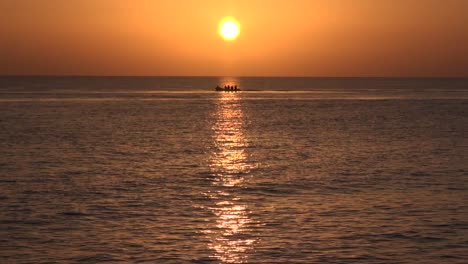 Tiro-Largo-Como-Motor-De-Barco-Lentamente-A-Través-De-La-Puesta-De-Sol-Naranja