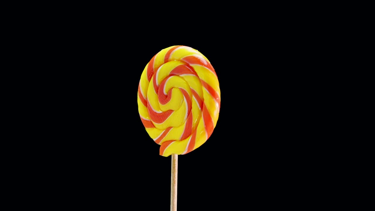 Lecca-lecca colorato che gira su sfondo nero. Caramella su bastoncino.