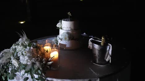 beautifully decorated wedding cake, candles, and champagne bucket on a table lit softly in the night