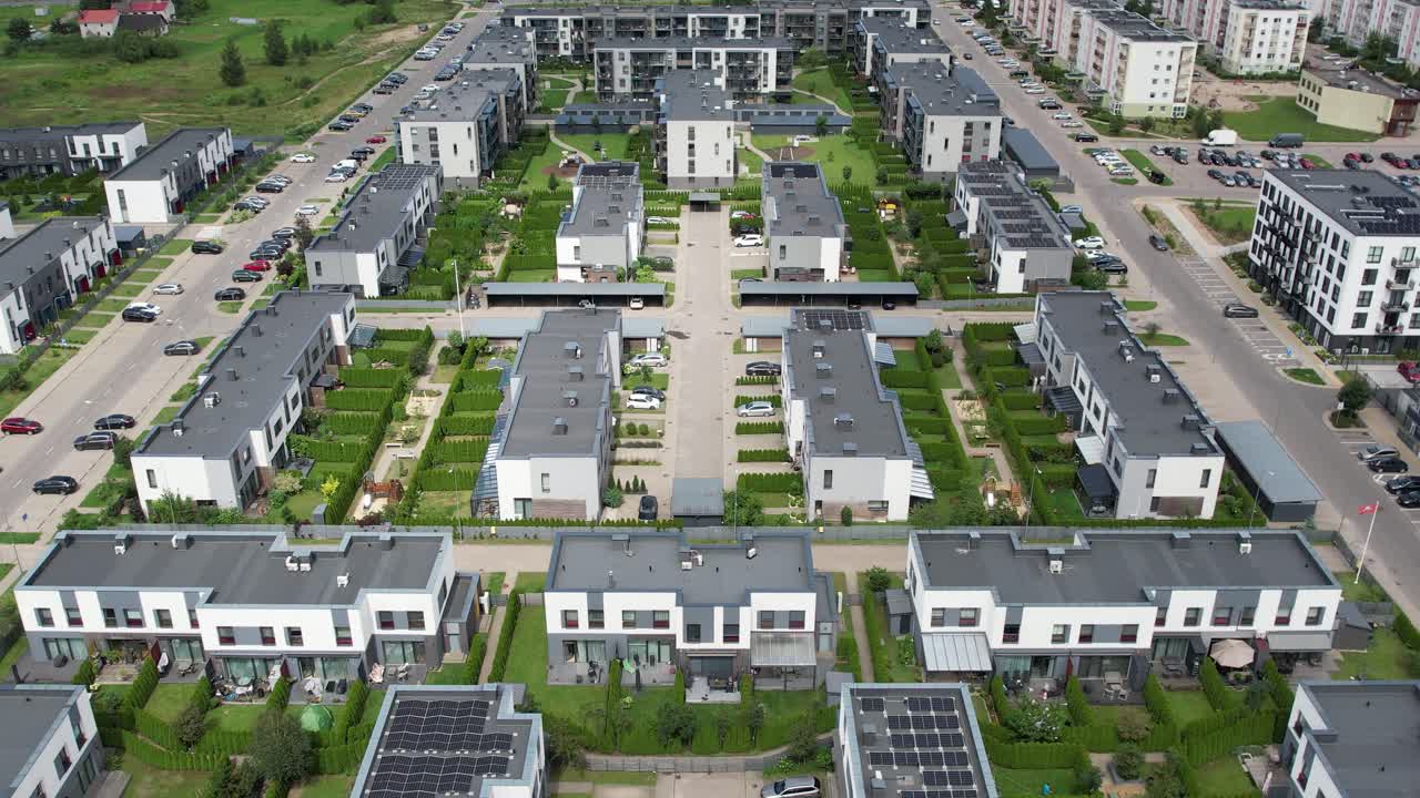 Aerial drone view of modern suburban housing, showing neatly arranged townhouses, solar panels, green courtyards, and organized streets in a contemporary Baltic neighbourhood