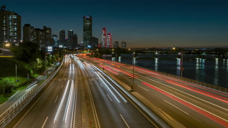 Timelapse-De-Seúl:-Tráfico-Nocturno-De-Automóviles-En-La-Autopista-Olímpica-Durante-La-Hora-Pico-Con-Vista-Al-Rascacielos-Del-Edificio-63-En-El-Distrito-Financiero-De-Yeouido,-Corea-Del-Sur