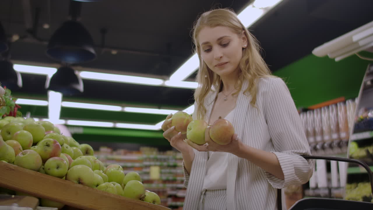 Attractive young woman choosing apple at fruit vegetable supermarket marketplace