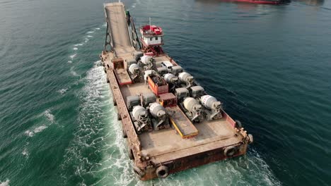 Barge-loaded-with-Concrete-mixer-trucks-pulled-to-port-by-a-Tugboat-in-Hong-Kong-bay,-Aerial-view