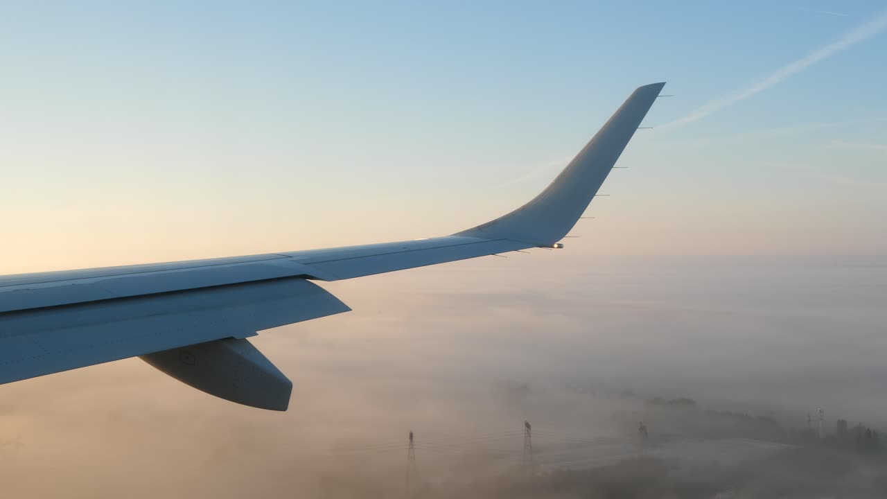 vista del pasajero del ala del avión y el ala contra el cielo del atardecer mientras se acerca a aterrizar en la niebla