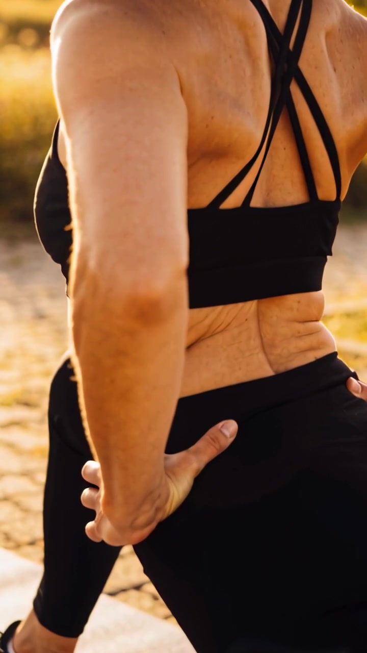 Video verticale: Inspirando, donna che si riscalda con stretching per le anche sulle dune, in reggiseno sportivo, leggings, tappetino