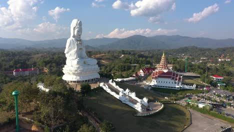 amazing backwards aerial drone of wat huay pla kang giant white big statue and pagoda temple with mountains and landspace in chiang rai, thailand