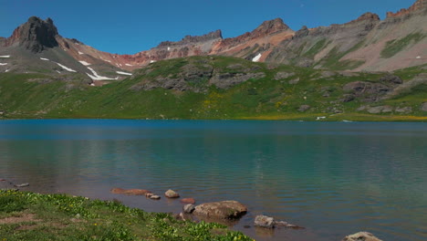 dreamy heavenly silverton ice lake basin aerial drone cinematic unreal deep sky blue wildflower shoreline silverton colorado lush green summer incredible snow melting rocky mountains slide left