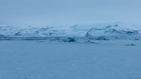 Aerial-landscape-view-of-the-frozen-Jokulsarlón-lake-area,-with-icebergs-covered-in-snow,-in-Iceland,-at-dusk