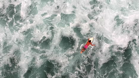 top view of male surfer lying and swimming on a surfboard afloat on wavy ocean surface in la ticla, mexico