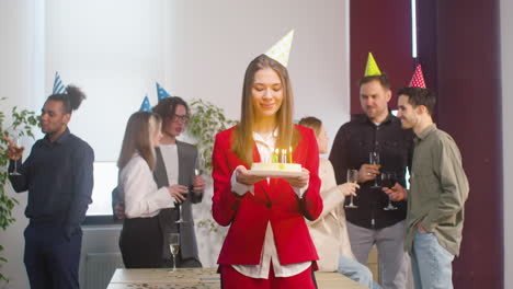 retrato de una bella mujer sosteniendo un pastel de cumpleaños y mirando a la cámara durante una fiesta en la oficina 2