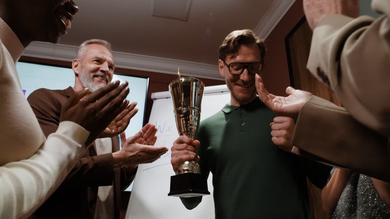Man receiving a trophy and handshake from a colleague, celebrated by clapping team members