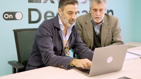 Partners discussing which workers they will dismiss while using laptop