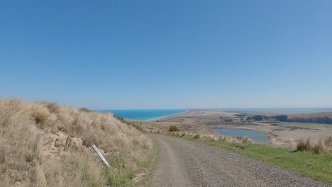 Pov-Off-road-Ciclismo-Cuesta-Abajo-Con-Increíbles-Vistas-Del-Lago-Y-El-Océano-En-Un-Día-De-Verano---Bossu-Road,-Canterbury