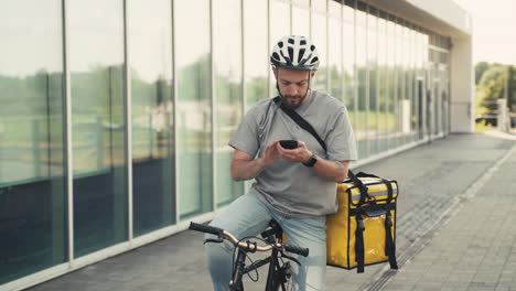 food delivery guy wearing thermal backpack uses the geolocator on his smartphone to navigate to the delivery location riding a bike