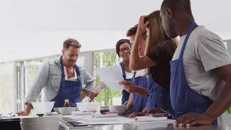 female teacher with male student mixing ingredients for recipe in cookery class in kitchen