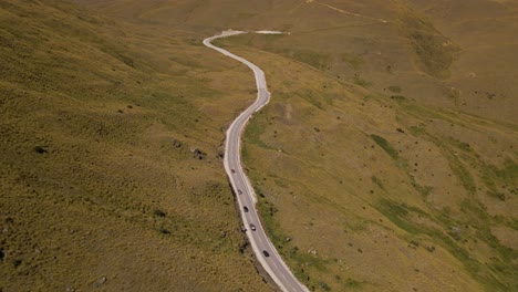 Cars-driving-up-Cardrona-Mountain-Pass-in-Otago,-New-Zealand---aerial-tilt-up