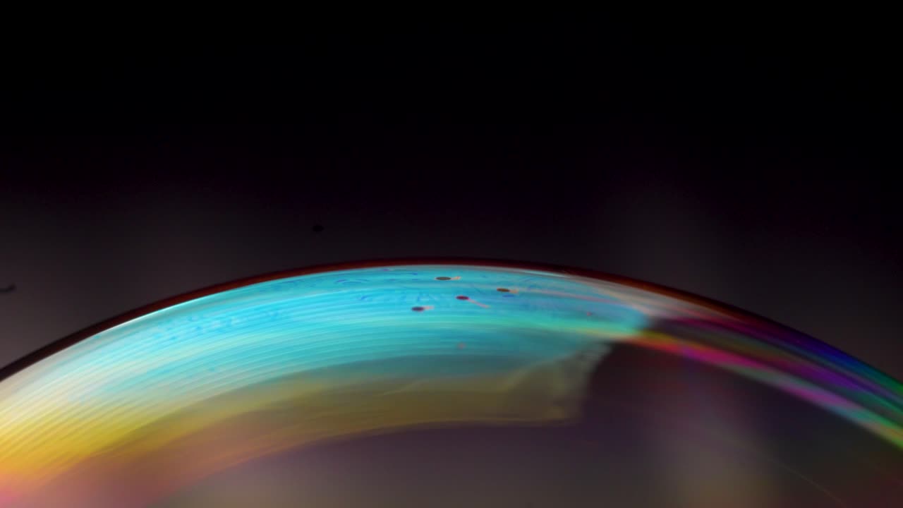 Experience soap bubbles in macro view, revealing complex designs resembling celestial nebulae against vibrant backgrounds.