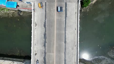 aerial top down view of mopeds and tricycles driving across small bridge above a dirty, shallow river in virac, catanduanes