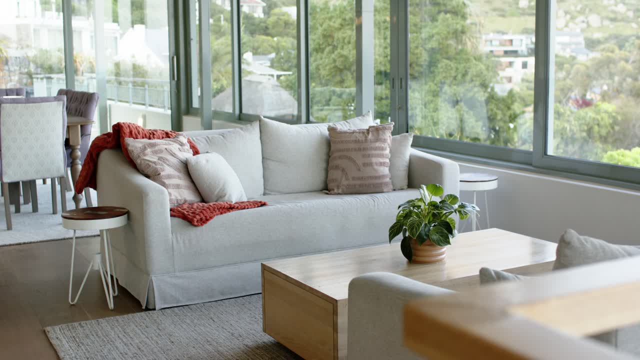 Shot beginning capturing white slipcovered sofa by floor-to-ceiling windows overlooking green hills