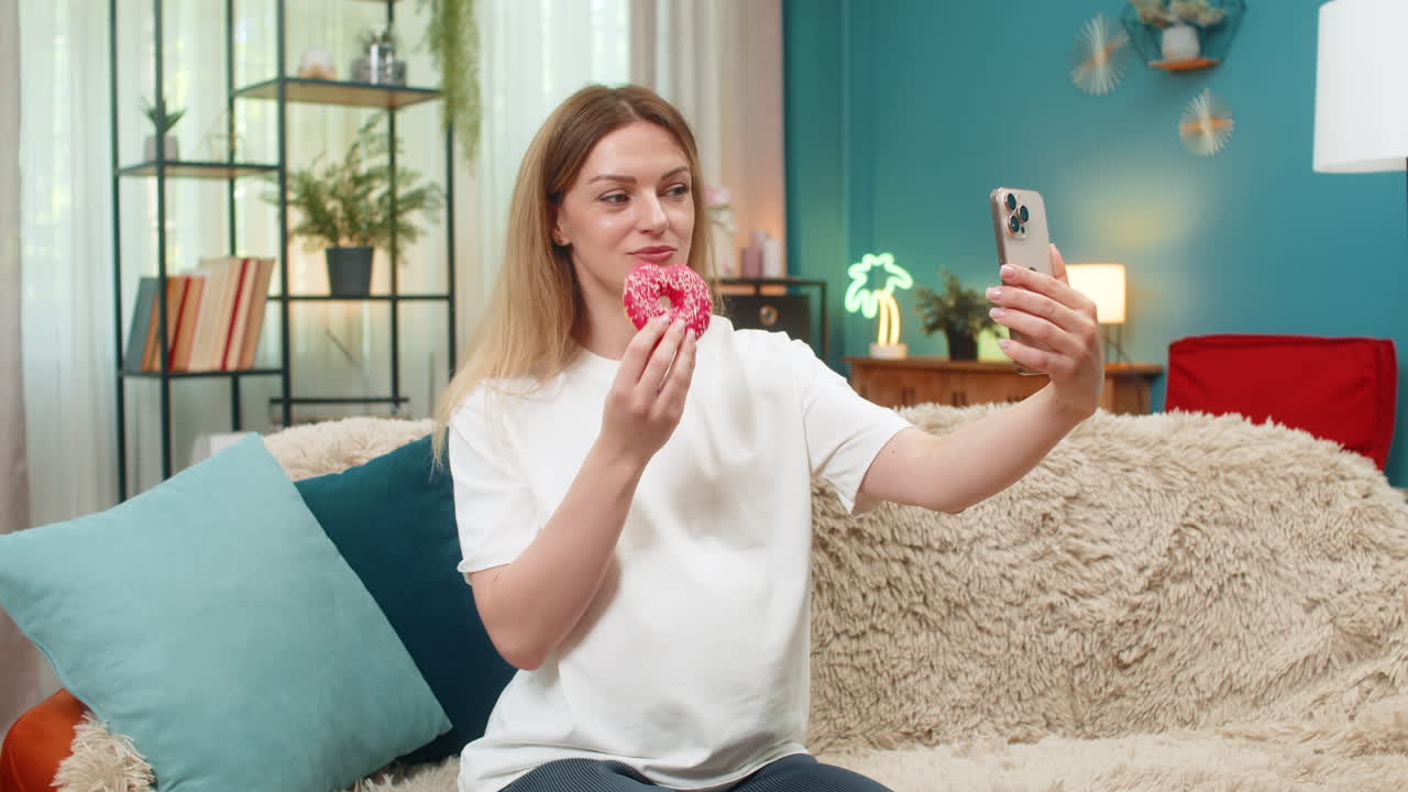 Pregnant woman bites pink donut selfie smartphone laughs enjoys sweet treat keeps fun memory forever