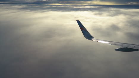 Wing-of-an-airliner-airplane-turning-above-the-clouds,view-from-passenger-seat