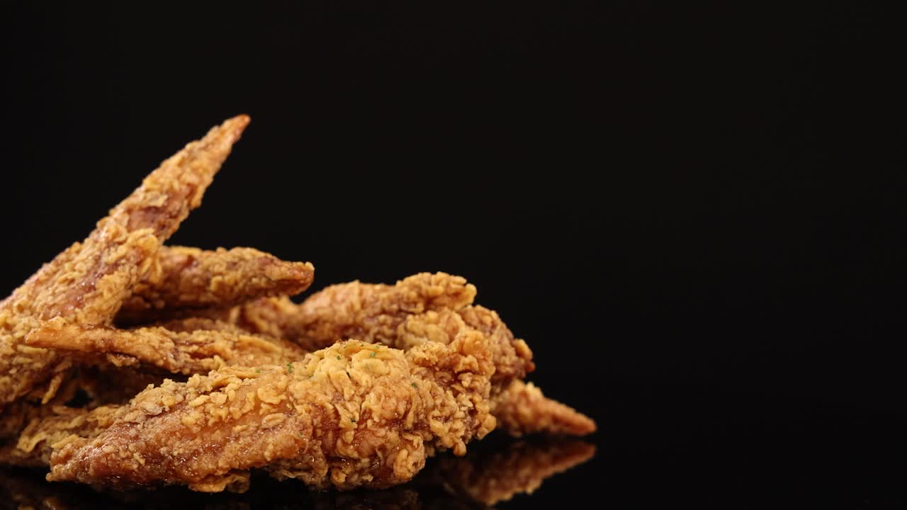 Golden-brown fried chicken wings rotate smoothly on a glossy black surface, illuminated by soft studio lighting, highlighting crunchy texture and appetizing detail
