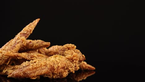 golden-brown fried chicken wings rotate smoothly on a glossy black surface, illuminated by soft studio lighting, highlighting crunchy texture and appetizing detail